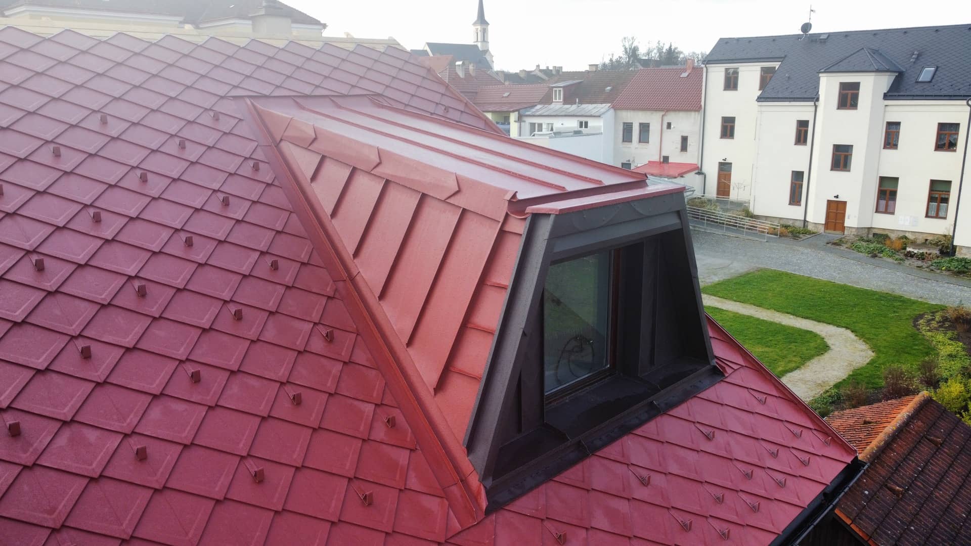 Pohled na jedno z oken na opravené červené střeše obsahující falcovanou šablonu v tmavě černé barvě.